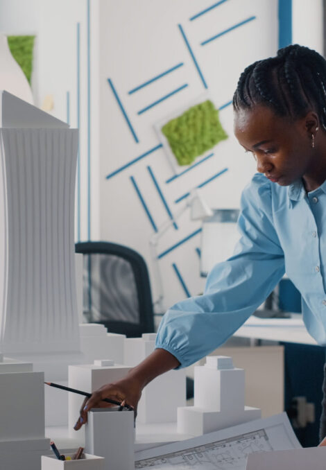 African american woman analyzing blueprints plan and building model to work on architecture. Architect working with maquette and layout print to design urban construction for development.